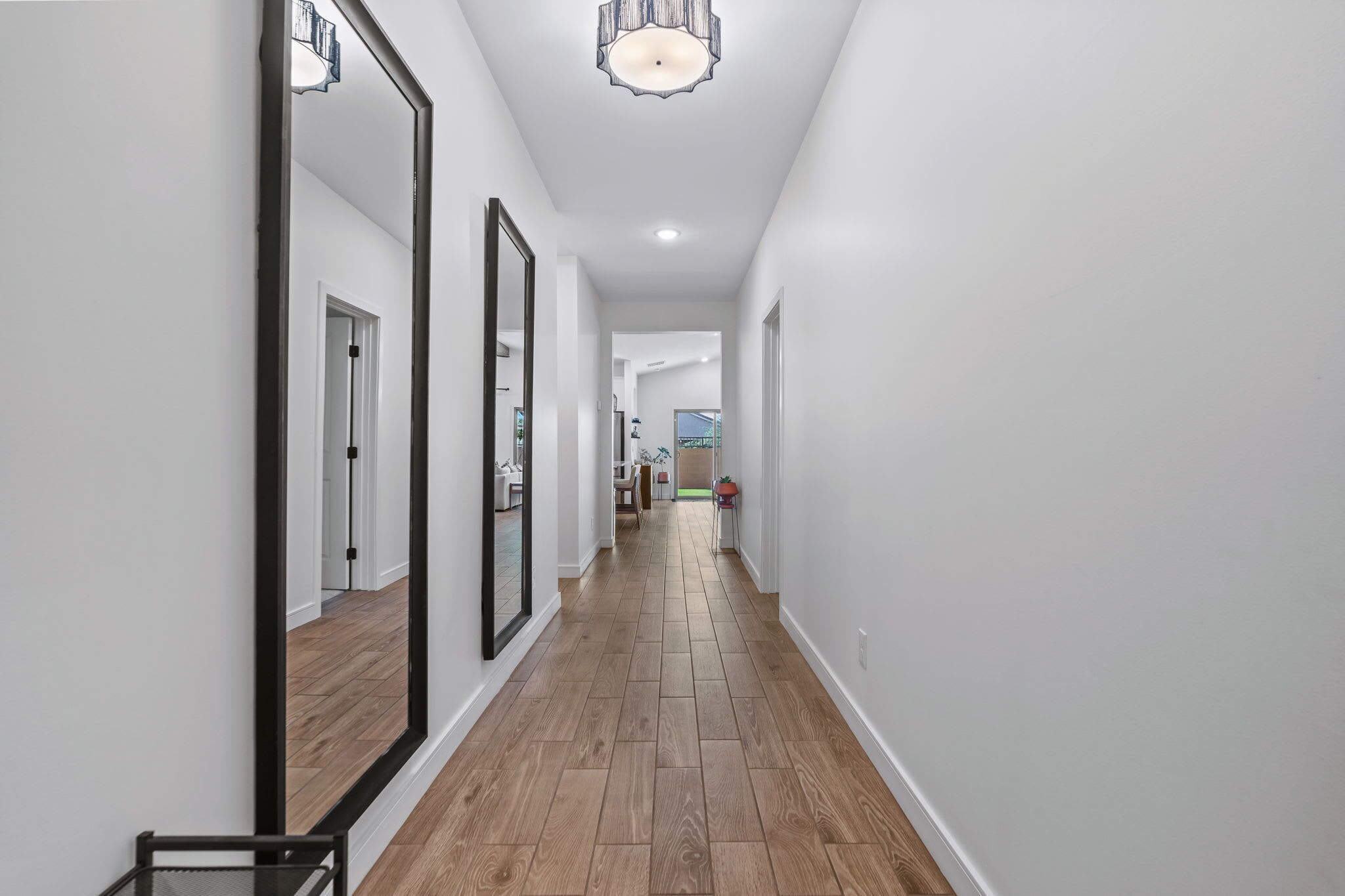 A hallway with wooden flooring, white walls, and large mirrors.
