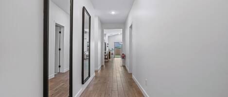 A hallway with wooden flooring, white walls, and large mirrors.