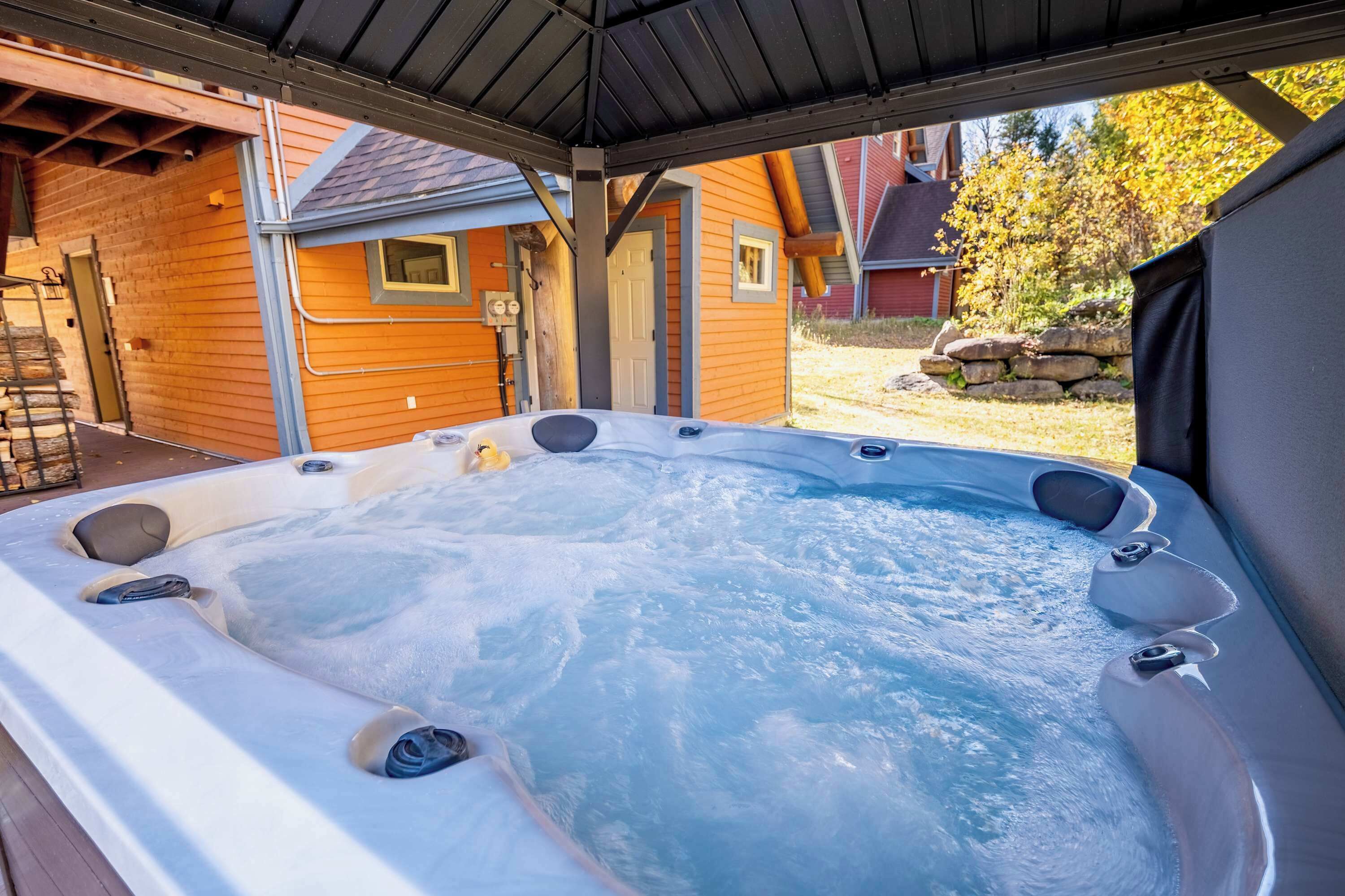 Un bain à remous situé sous une zone abritée, avec une maison en bois en arrière-plan.