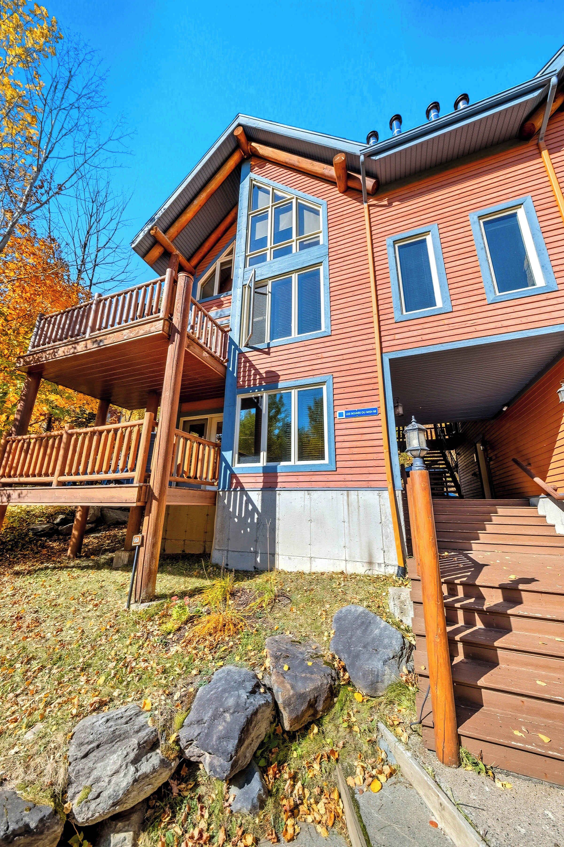 Un immeuble à plusieurs étages doté d’une terrasse en bois et d’un escalier menant à l’entrée.