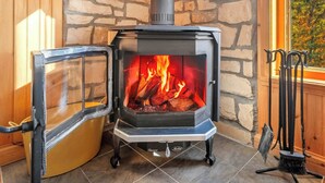 En vedeldad kamin med en vägg av sten som bakgrund, ett fönster med utsikt och en dörr av trä.