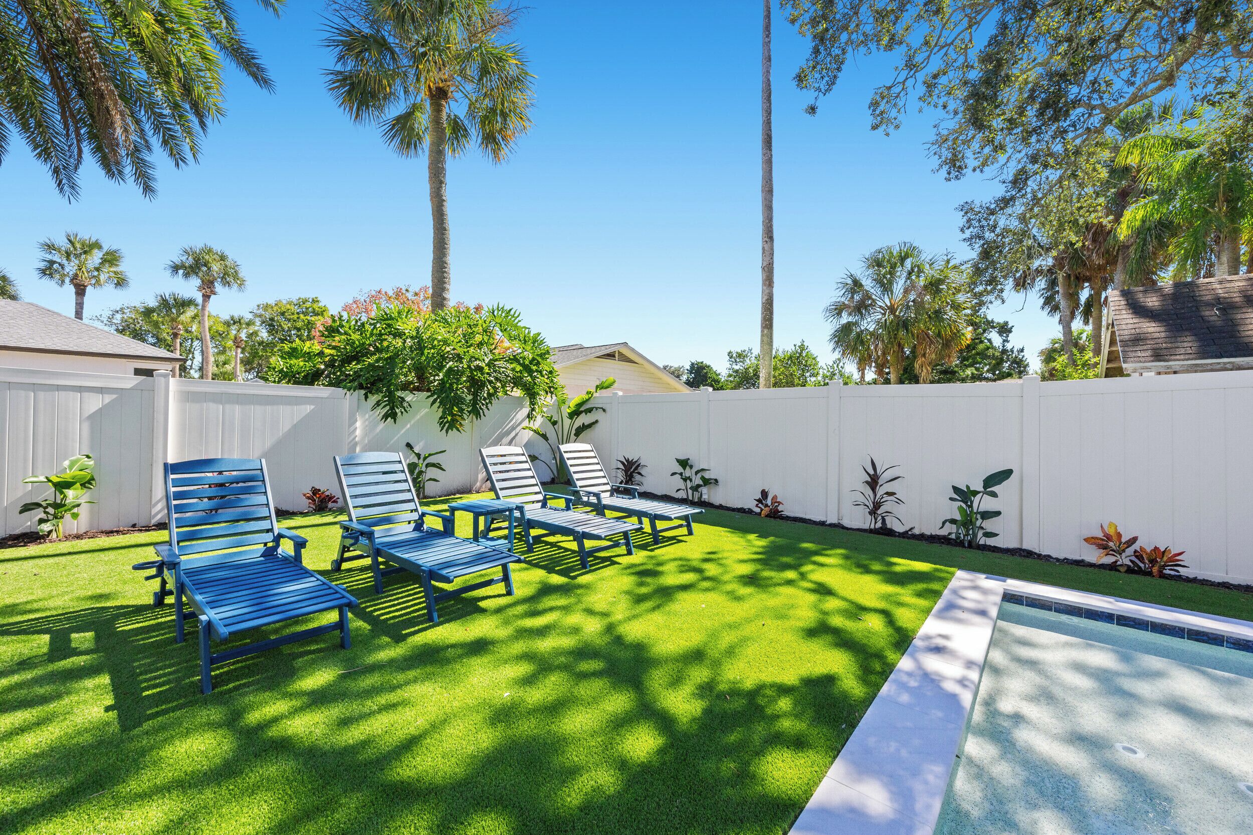 Ein Garten mit Pool, grünem Kunstrasen und blauen Liegestühlen.