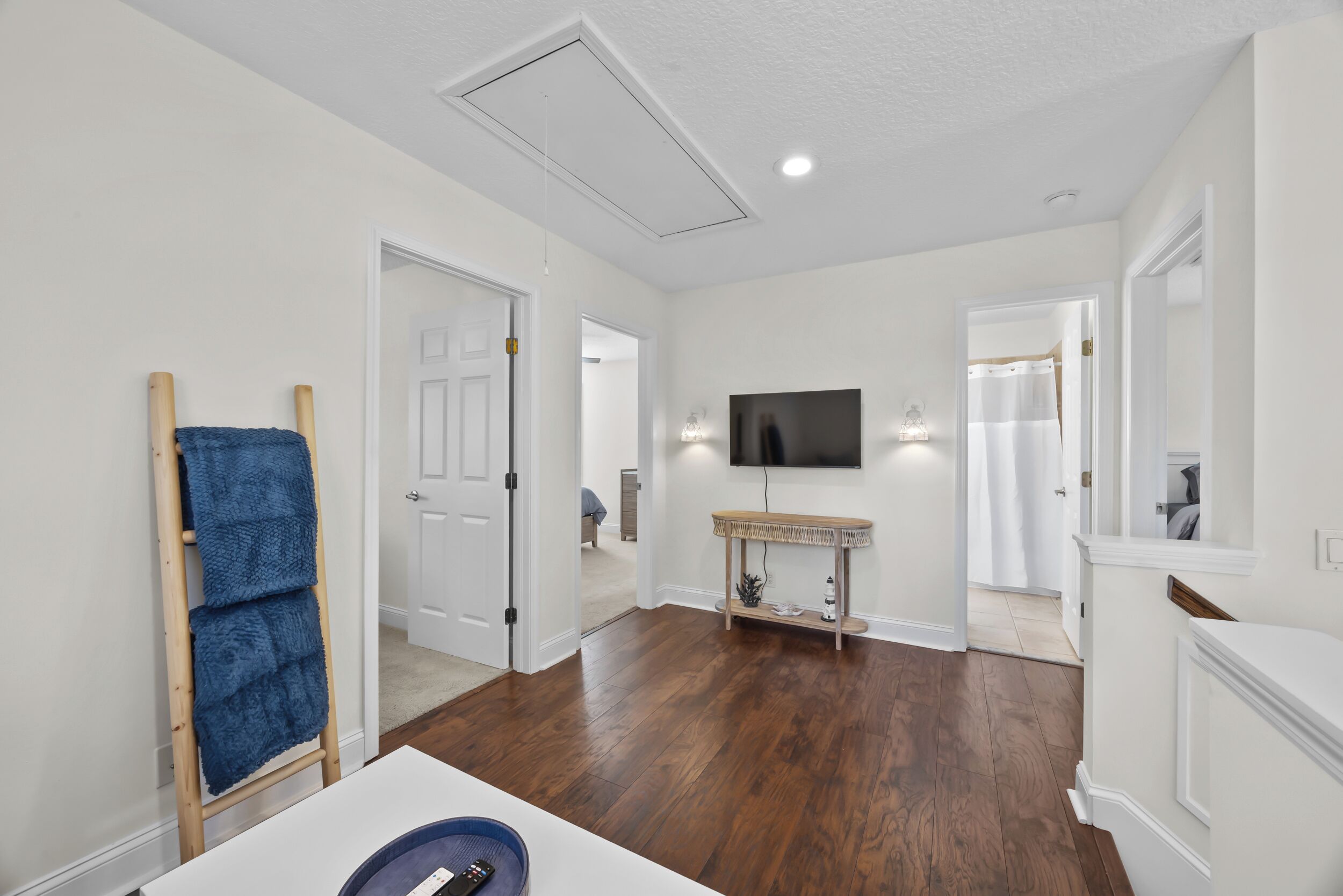 A spacious room with hardwood flooring, a mounted TV, and a large mirror.