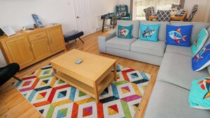 Un salon comprenant un canapé, une table basse, un téléviseur, un meuble en bois et un tapis coloré.