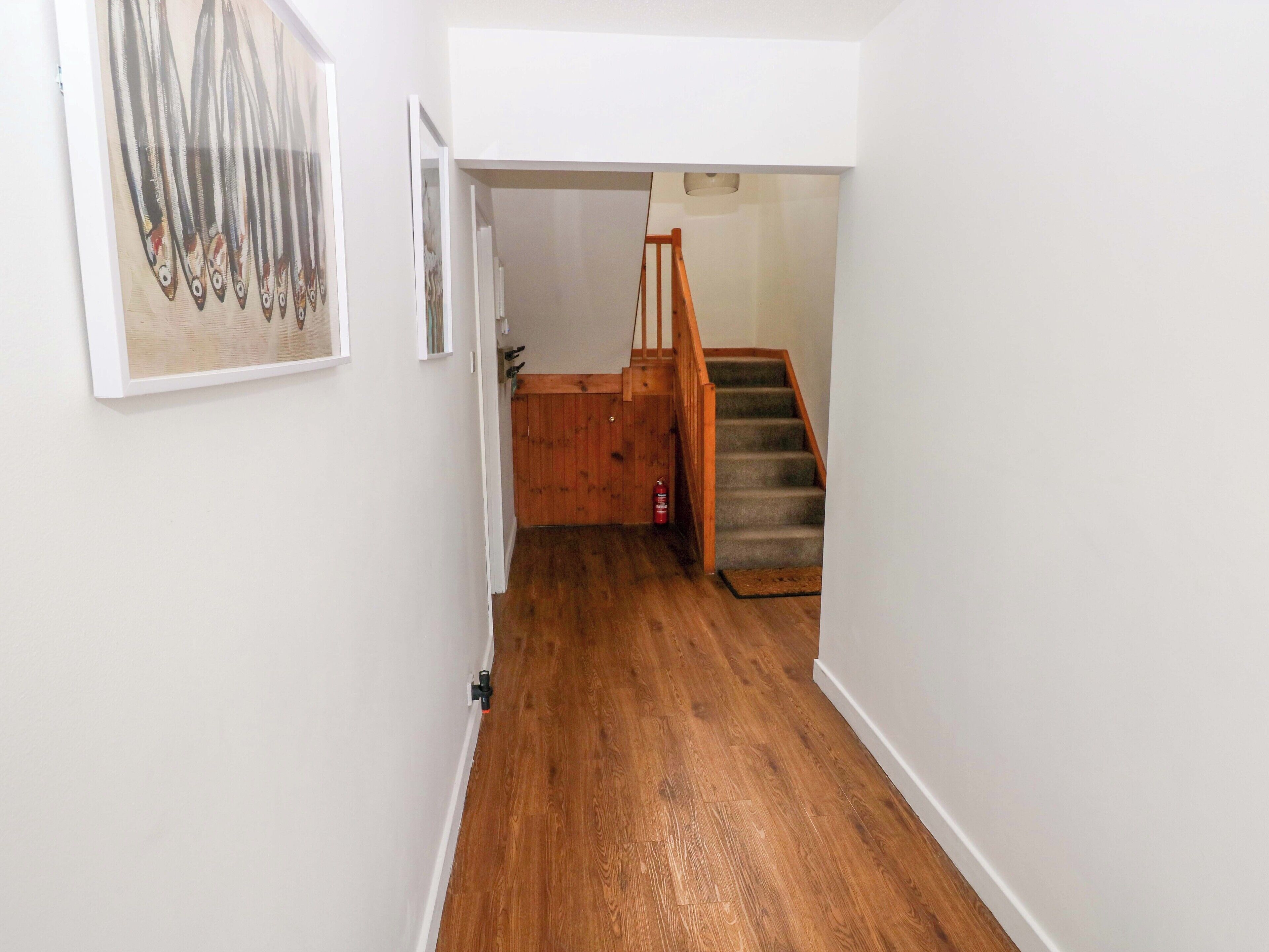 A hallway with wooden flooring, a staircase with wooden railings, and a framed artwork on the wall.