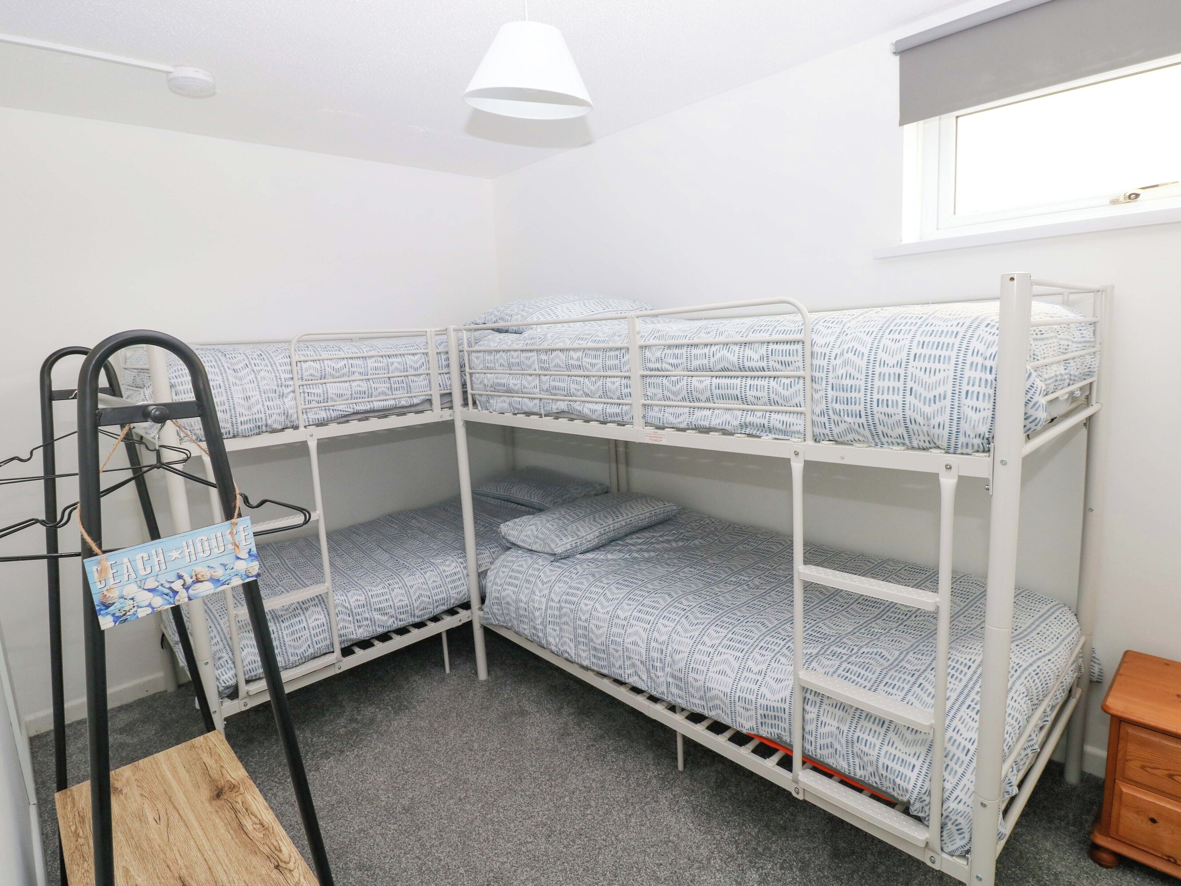 A bunk bed room with a wooden ladder, a small wooden table, and a window with a blind.