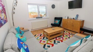 Un salon comprenant un canapé, une table basse, un fauteuil, un téléviseur et une fenêtre donnant sur un beau paysage.