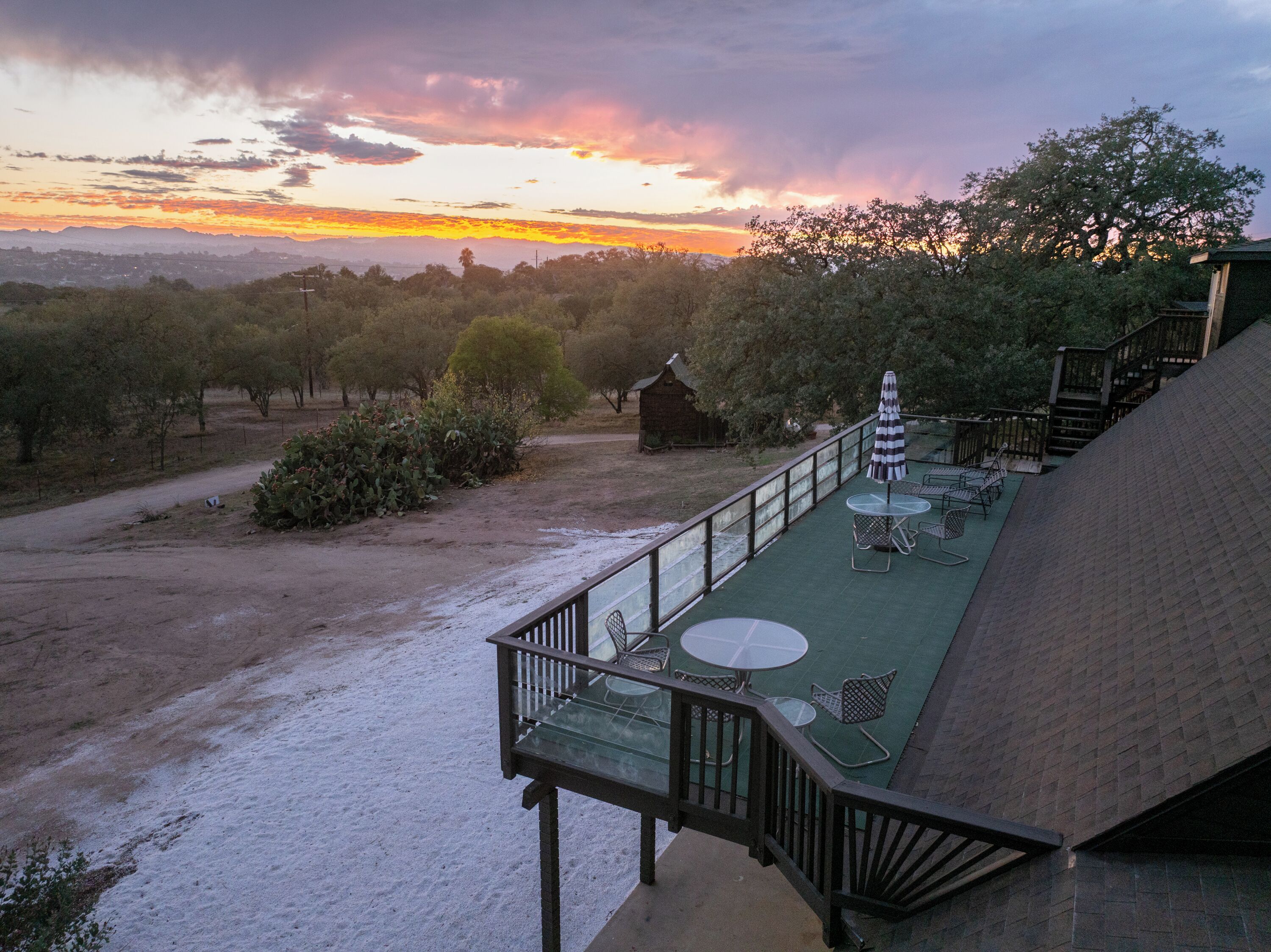 Una terraza con mesas al aire libre, con vistas a un paisaje de árboles y un atardecer distante.