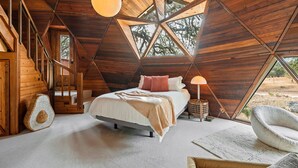 Une chambre confortable avec un plafond en bois, un lit avec des oreillers, une lampe et une vue sur les arbres par la fenêtre.