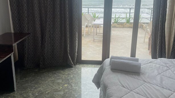A hotel room with a bed, a desk, and a view of the sea through a sliding glass door. - Palolem Sea n' Sand Beach View   (Canacona)