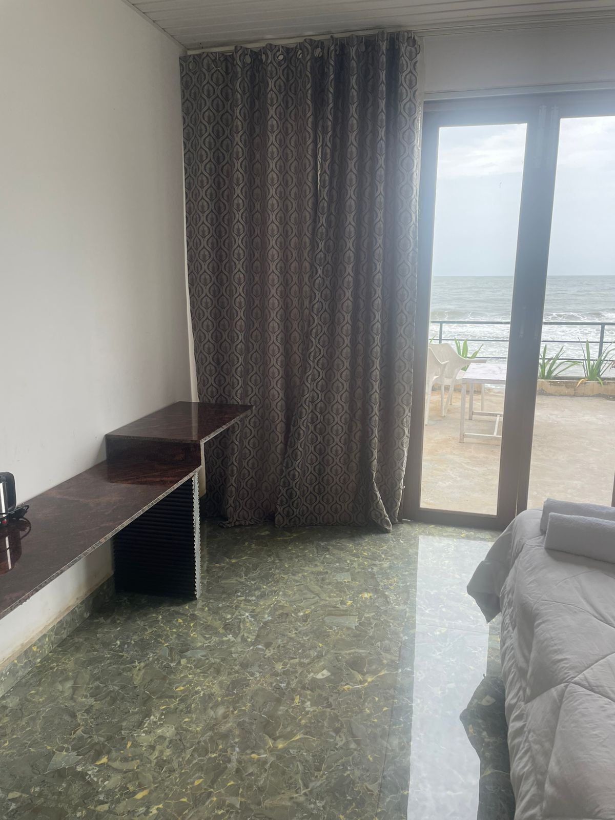 A hotel room with a bed, a desk, and a view of the sea through a large window.