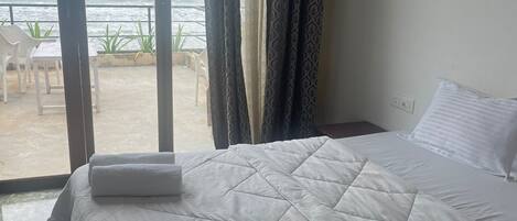 Une chambre d’hôtel avec un lit, une vue sur la mer et un balcon équipé de chaises.