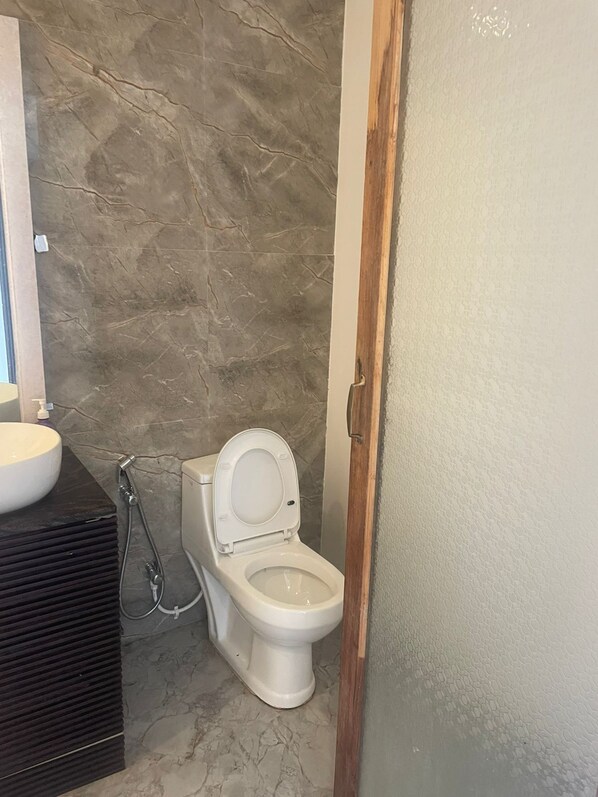 A bathroom with a marble wall, a white toilet, and a black vanity with a white sink.