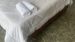 A neatly made bed with a quilted white duvet, a wooden nightstand, and a rolled white towel. - Palolem Sea n' Sand Beach View   (Canacona)