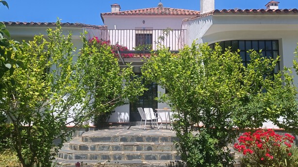 A white building with a red-tiled roof, stone steps leading to a balcony, and lush green foliage. - Esperanza's little house (Aracena)