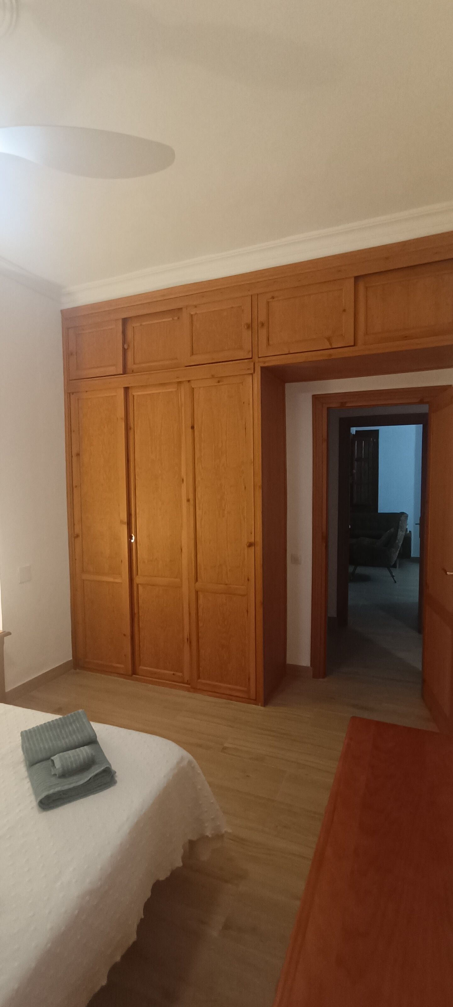 Une chambre avec une grande armoire en bois, un lit recouvert d’une courtepointe blanche et un plancher en bois.