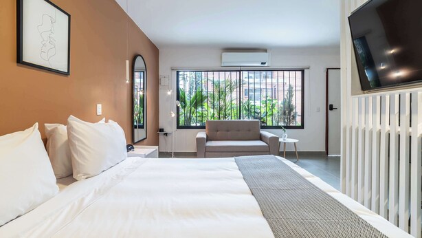 Une chambre d’hôtel avec un grand lit, un canapé, une télévision et une fenêtre donnant sur un paysage verdoyant.