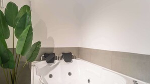 Une salle de bain moderne avec une baignoire blanche, une plante en pot et un porte-serviettes.