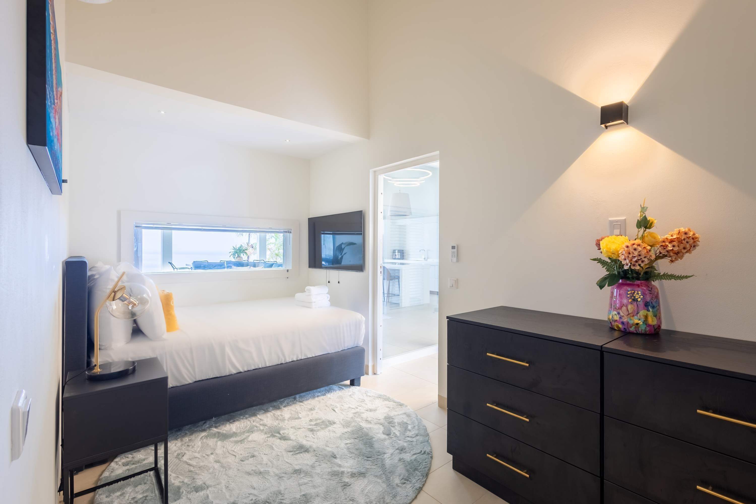 A modern bedroom with a bed, bedside table, dresser, and a TV mounted on the wall.