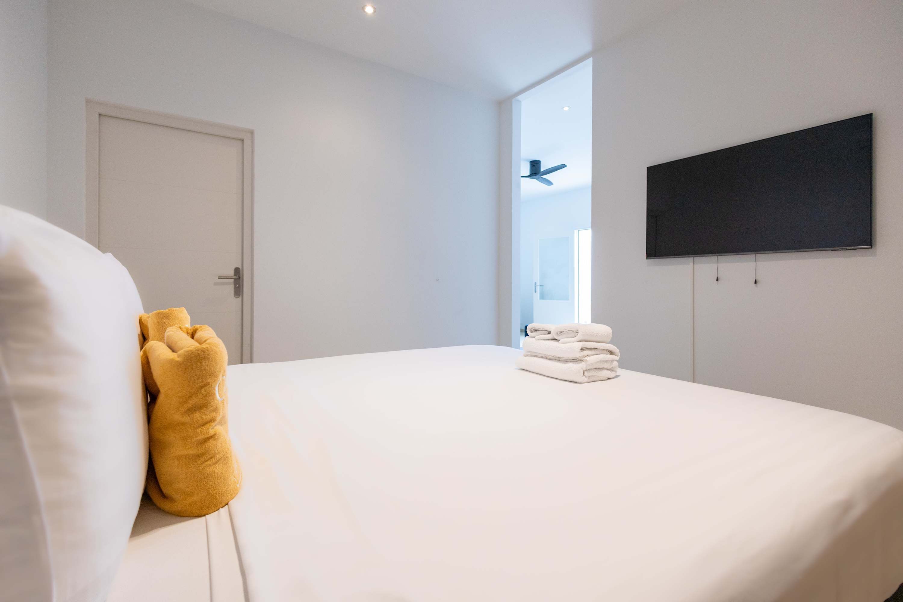 A hotel room with a bed, a flat-screen TV mounted on the wall, and a door.