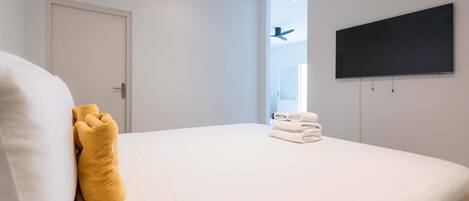 A hotel room with a bed, a flat-screen TV mounted on the wall, and a door.