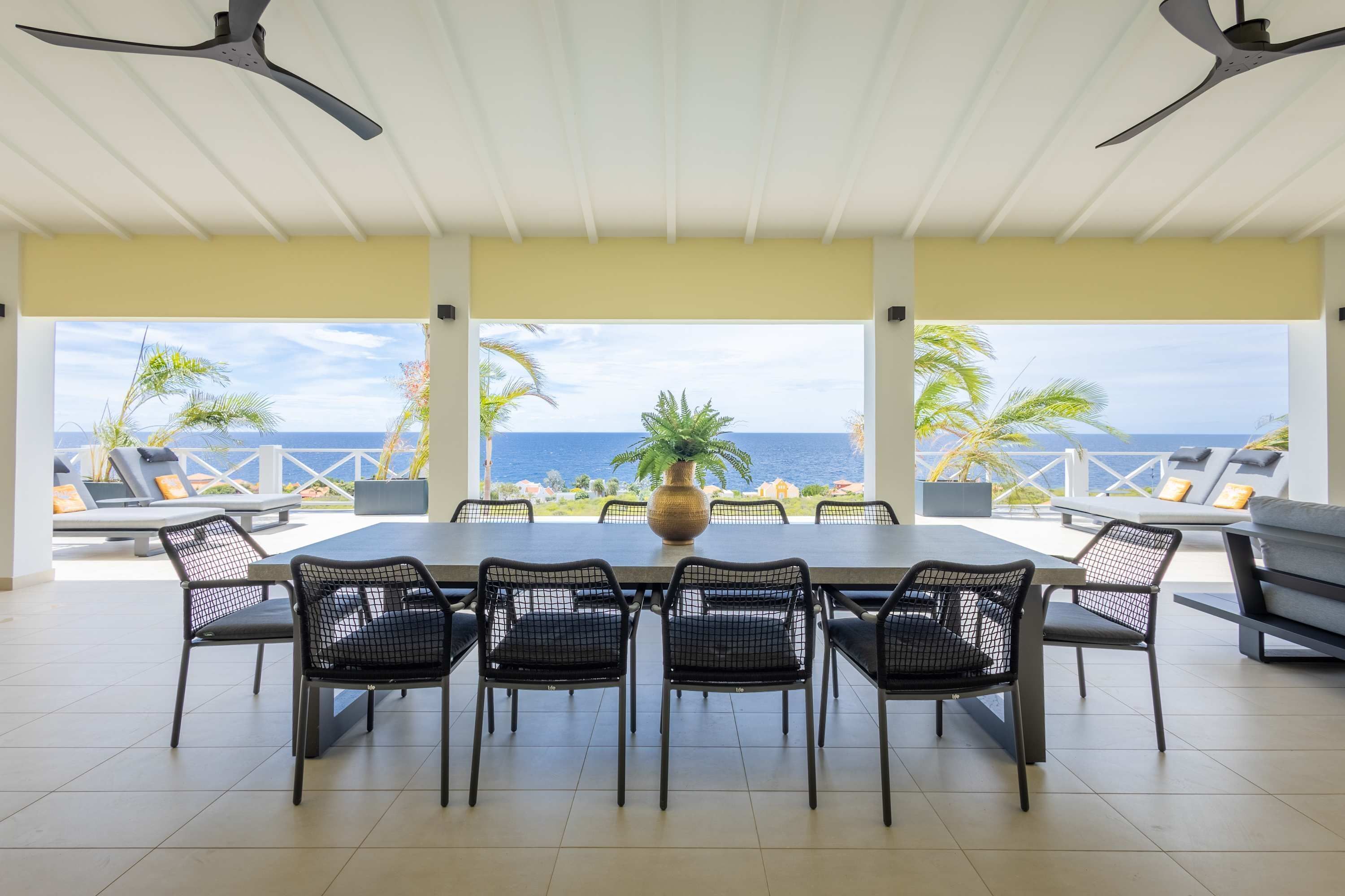 A dining area with a table and chairs, a potted plant, and a view of the ocean.