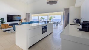Ein modernes Wohnzimmer mit einer zentralen Kochinsel, einem Flachbildfernseher und Meerblick.