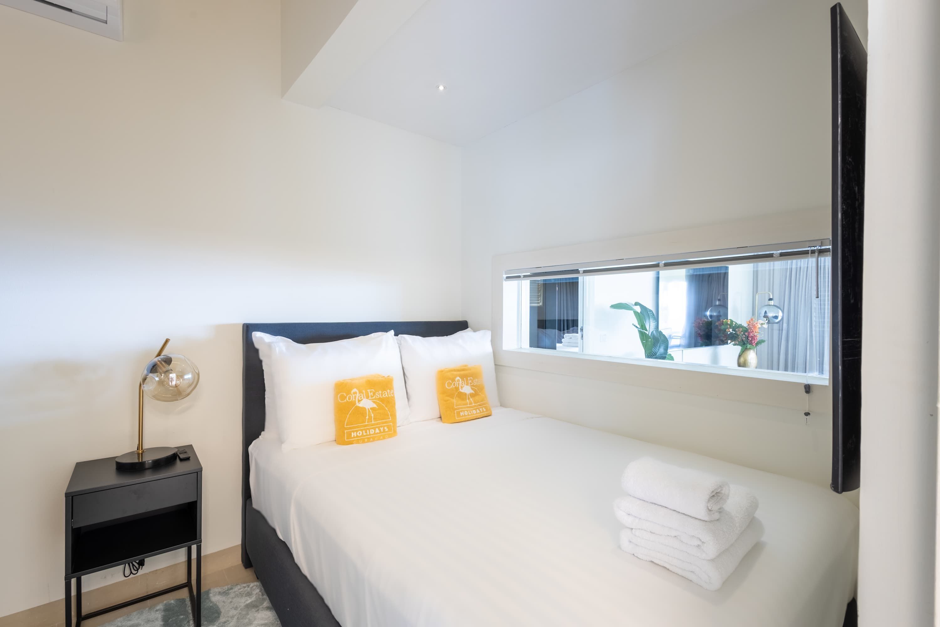 Quarto de hotel com cama, mesa de cabeceira, abajur e janela com vista para o exterior.