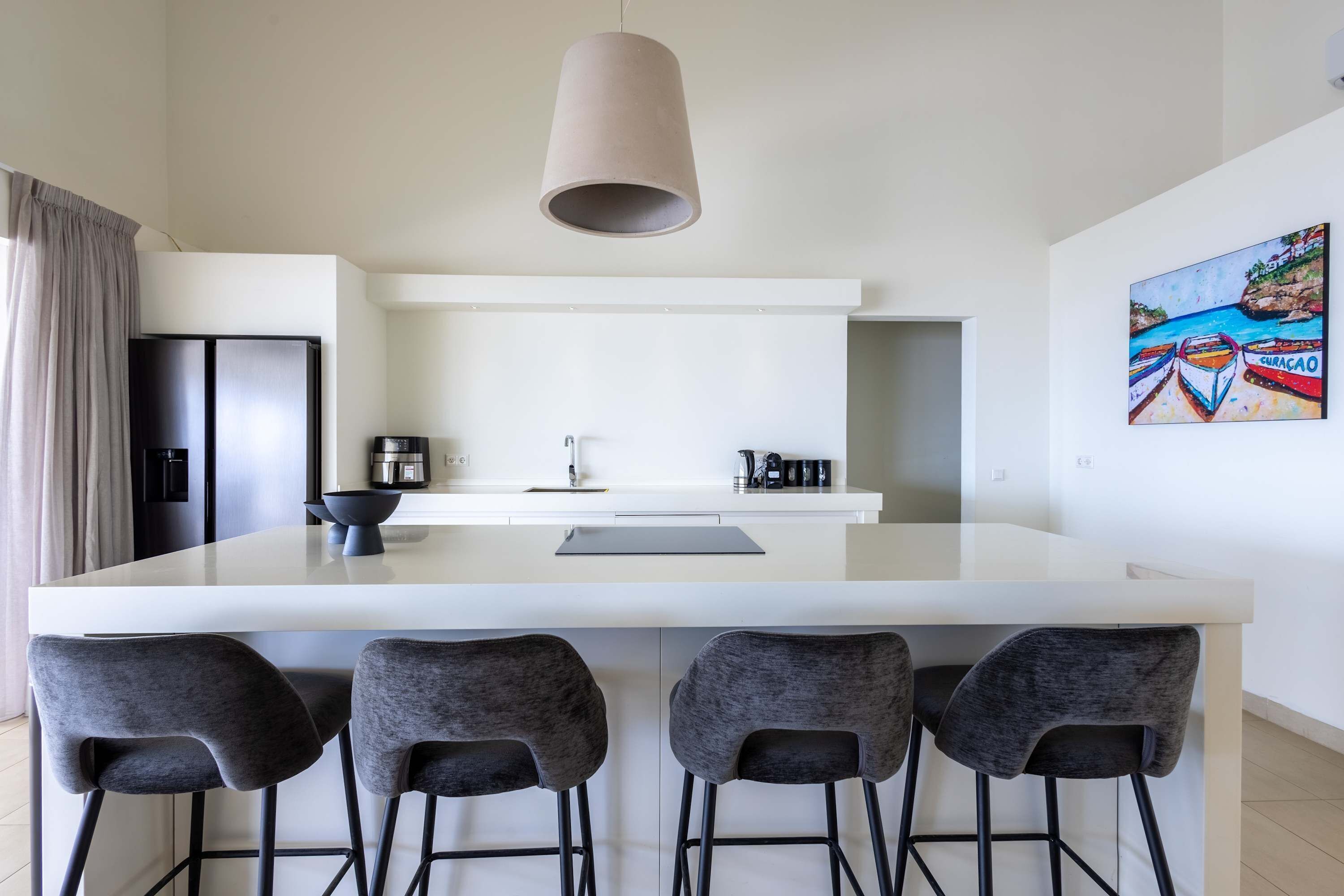 Een moderne keuken met een centraal eiland, vier barkrukken, een hanglamp en een kleurrijk schilderij aan de muur.