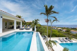 Un espace piscine avec des chaises longues et vue sur l’océan.