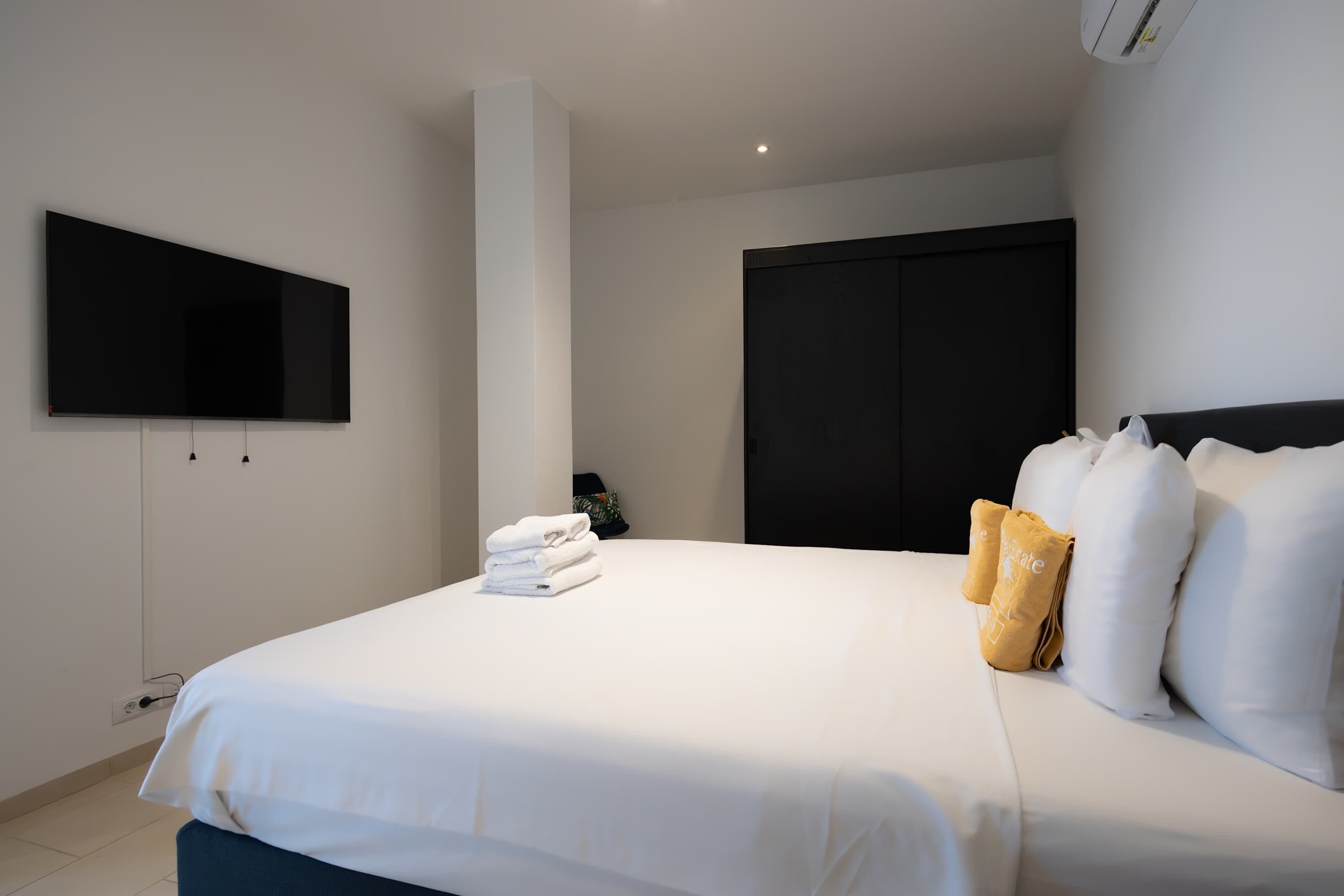 Une chambre d’hôtel moderne avec un grand lit, un téléviseur à écran plat fixé au mur, une armoire et une petite plante sur la table de chevet.