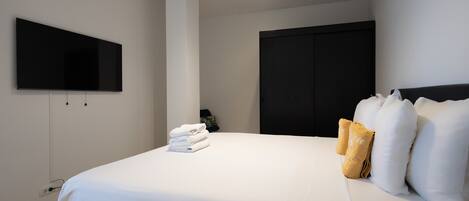 Une chambre d’hôtel moderne avec un grand lit, un téléviseur à écran plat fixé au mur, une armoire et une petite plante sur la table de chevet.
