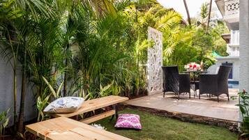 Une terrasse avec une table et des chaises en bois, entourée d’une végétation luxuriante et d’une clôture blanche décorative.
