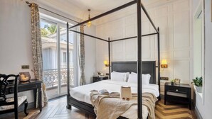 A four-poster bed with a white bedspread, two bedside tables with lamps, a wooden floor, and a view of the outdoors through a glass door. - Luxury 4bhk Pool Getaway in North Goa Villa Kaia (Valpoy)