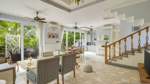 A spacious living area with a dining table, chairs, a staircase, and a view of greenery outside. - Luxury 4bhk Pool Getaway in North Goa Villa Kaia (Valpoy)
