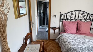 Een slaapkamer met een bed, een houten stoel, een spiegel en een deur naar een badkamer.