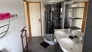 Een moderne badkamer met douchecabine, dubbele wastafels en een grote spiegel.