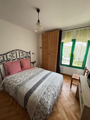 Une chambre à coucher avec un lit, une armoire en bois, un bureau et une fenêtre avec des rideaux.