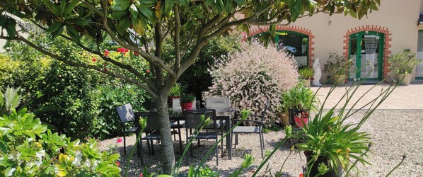 Ein Gartenbereich mit Tisch und Stühlen, umgeben von Pflanzen und einer Statue.