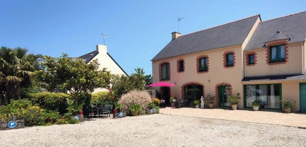 Ein zweistöckiges Haus mit Kiesweg, Garage und einer Terrasse mit Sitzgelegenheit.