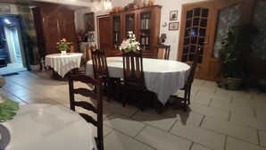 Un coin repas avec une table ronde, des chaises et une nappe blanche. On y trouve un meuble avec des portes en verre et une plante en pot.