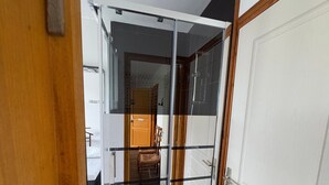 Un couloir avec une cloison en verre, une porte en bois et un escalier menant à une autre pièce.