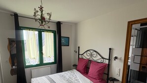 Une chambre à coucher avec un lit, une fenêtre avec des rideaux, un radiateur, une petite table et une chaise.