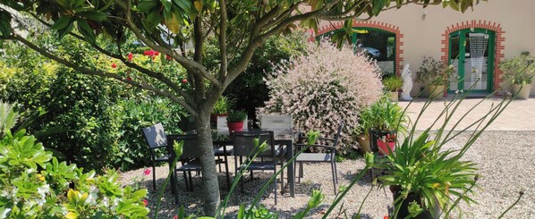 Ein Gartenbereich mit Tisch und Stühlen, umgeben von Pflanzen und einer Statue.