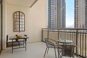 A balcony with a table and chairs, a window with a wooden frame, and tall buildings in the background. - Creekside 18 A - 103 2BD (Dubai)