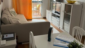 A compact living space with a sofa, a dining table with chairs, a small kitchenette, and a balcony with a railing. - La Casa Bonita (Benalmádena)