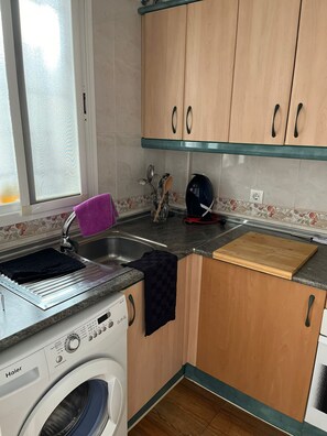 A compact kitchen with a washing machine, a sink, and wooden cabinets. - La Casa Bonita (Benalmádena)