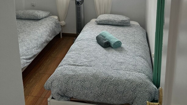 A bedroom with two beds, a ceiling fan, a window with sheer curtains, and a radiator. - La Casa Bonita (Benalmádena)