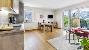 A modern kitchen with wooden cabinets, a dining area with a table and chairs, and a large sliding glass door leading to a garden. - Holiday Apartment 'Amsel A, 50 sqm' with Mountain View, Private Terrace and Wi-Fi (Lennestadt- Saalhausen)