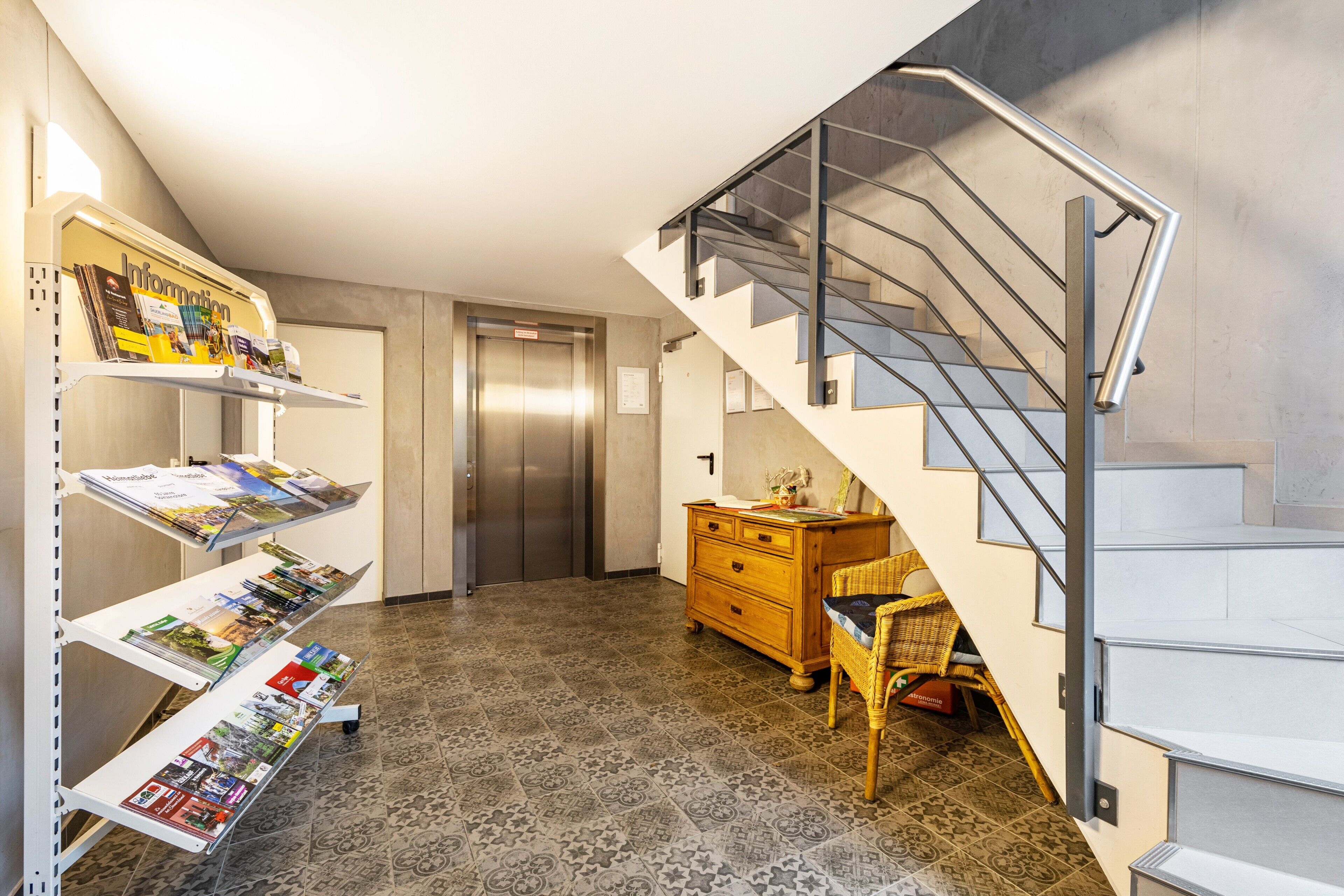A modern interior with a staircase, a wooden dresser, and a wall-mounted information shelf.